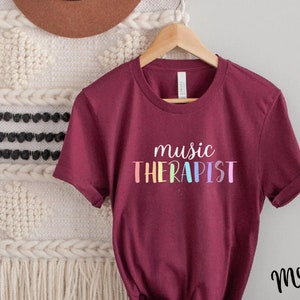 May include: Maroon t-shirt with the text "music THERAPIST" in rainbow colors.