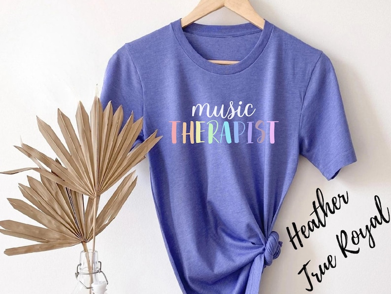 May include: A purple t-shirt with the text "music therapist" in rainbow colors. The text is in a playful, handwritten font.