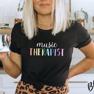 May include: A black t-shirt with the text "music therapist" in rainbow colors. The text is in a playful, handwritten font.