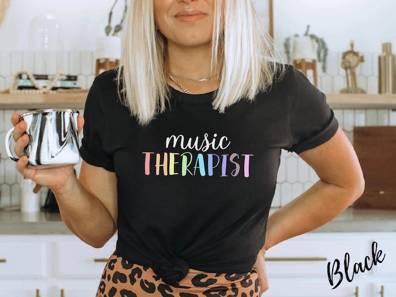 May include: A black t-shirt with the text "music therapist" in rainbow colors. The text is in a playful, handwritten font.