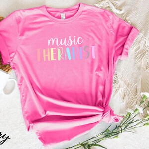 May include: Pink t-shirt with the text "music therapist" in rainbow colors.