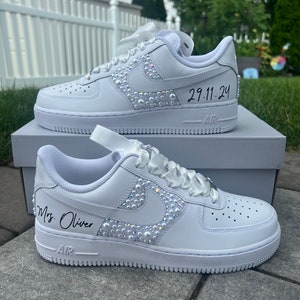 Puede incluir: Zapatillas blancas de cuero con un dise&ntilde;o de perlas y diamantes de imitaci&oacute;n en el swoosh. Las zapatillas tienen una cinta blanca atada alrededor y el texto "Mrs. Oliver" y "29.11.24" escrito en ellas.