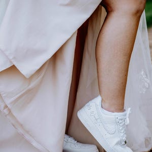 K&ouml;nnte beinhalten: Eine Braut in einem wei&szlig;en Hochzeitskleid und wei&szlig;en Turnschuhen mit dem Text "Mrs. Wonderful" auf einem Schuh.