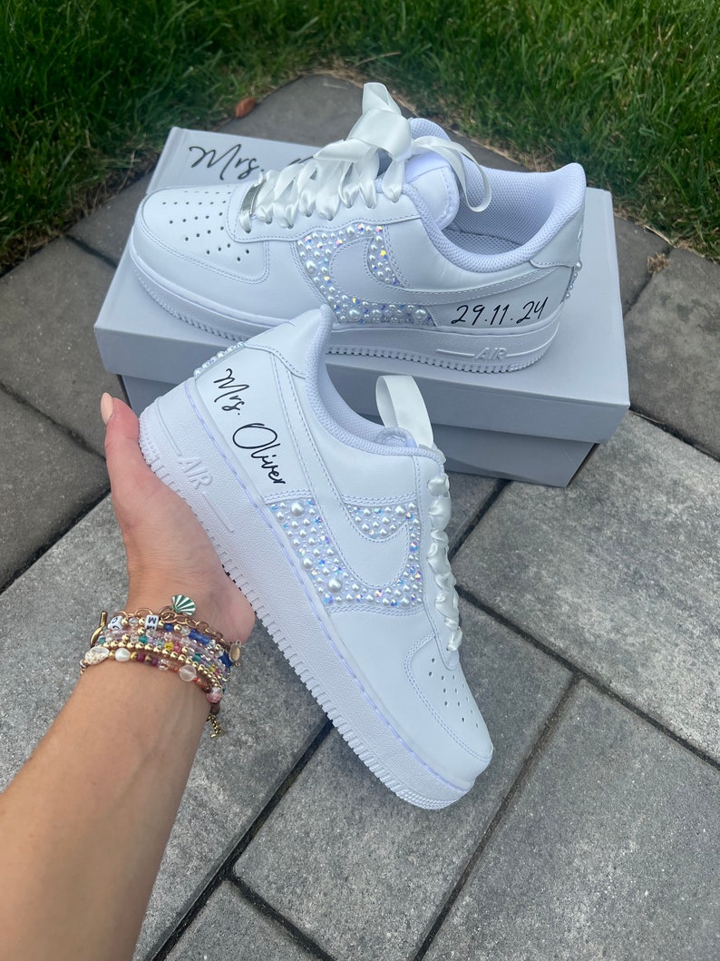Puede incluir: Zapatillas blancas de cuero con una cinta de sat&eacute;n blanca atada alrededor del tobillo. Las zapatillas est&aacute;n decoradas con diamantes de imitaci&oacute;n y tienen el texto "Mrs. Oliver" escrito en el lateral. La fecha "29.11.24" est&aacute; escrita en el otro lado.