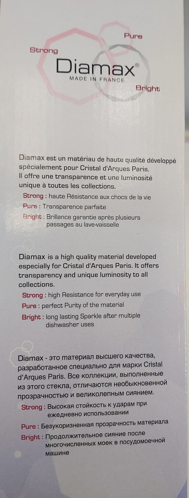 May include: A white label with the text "Diamax&reg; Made in France" in black. The label also features three overlapping circles in pink and gray with the words "Strong", "Pure", and "Bright" in red. The text below the circles describes the properties of the material Diamax, which is a high-quality material developed for Cristal d'Arques Paris.
