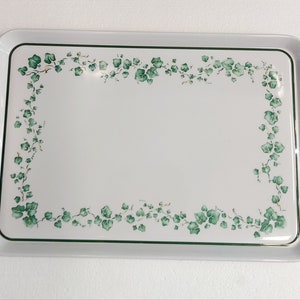 以下が含まれることがあります： 縁に緑のツタの葉のデザインが施された白いサービングトレイ。トレイには両側に2つのハンドルが付いています。