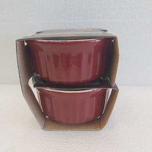 Op de afbeelding: Twee rode keramische ramekins in een kartonnen doos. De ramekins zijn geribbeld en hebben een wit interieur.