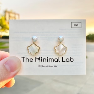 May include: A pair of stud earrings featuring a small white pearl top and a gold-rimmed, scalloped-edge mother-of-pearl flower charm. The earrings are displayed on a white card labeled S925 with the text The Minimal Lab and an Instagram icon.
