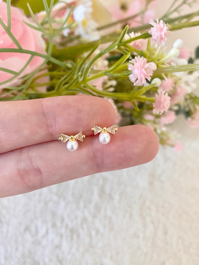 Puede incluir: Un par de pendientes de lazo de oro con peque&ntilde;as perlas blancas colgando de la parte inferior.