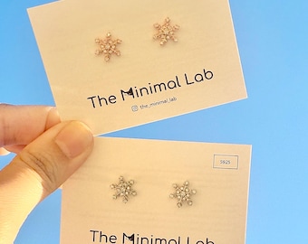 May include: Two pairs of snowflake-shaped stud earrings displayed on white cards labeled The Minimal Lab. One pair is rose gold-toned and the other is silver-toned, both featuring small clear stones. Each card includes the text S925 in a box.