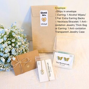May include: A brown paper envelope with a thank you sticker, a small brown gift envelope tied with twine, a necklace with a bear pendant on a card, and butterfly earrings in a clear case, accompanied by a list of included accessories.