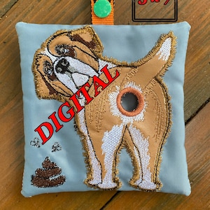 May include: A blue fabric dog poop bag holder with a brown and white embroidered dog design. The dog is facing away from the viewer and has a hole in its rear end. The text "DIGITAL" is written in red on the bag. The bag has a green paw print on the orange strap.