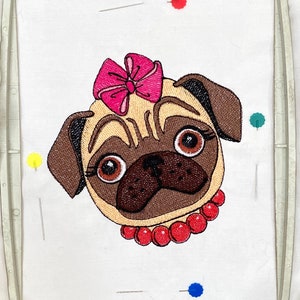 Può includere: Disegno ricamato di un carlino con un fiocco rosa e una collana di perle rosse. Il carlino guarda direttamente lo spettatore.