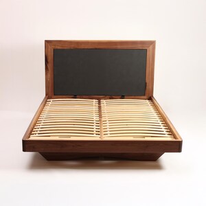 May include: A contemporary wooden bed frame featuring a dark headboard and a slatted base. The bed frame is crafted from dark brown wood and has a low profile design. The headboard is a solid black panel. The bed is empty, awaiting a mattress.