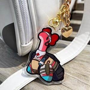 May include: A pink and red cartoon character with a medical cross on its chest and a stethoscope around its neck. The character is wearing a black vest and blue and white pants. The character is attached to a gold chain with a heart charm.