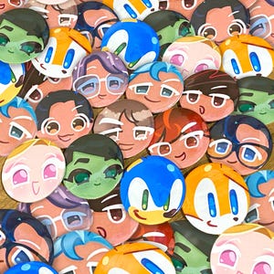 May include: A collection of colorful, round character buttons featuring various cartoon faces. The buttons showcase a variety of designs, including characters with blue, orange, and green skin, and some with glasses. The buttons are arranged closely together.