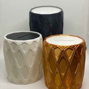 Puede incluir: Tres contenedores decorativos con un patrón de diamante. Los contenedores son negro, blanco y dorado.