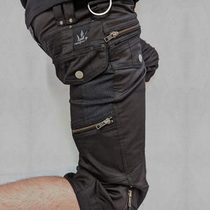 May include: Black cargo pants with multiple zippered pockets and a geometric pattern on the side. The pants are labeled "Quarter Pants Vortex" and "Indian Project".
