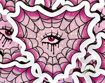 May include: Pink and black spiderweb sticker with a single red eye in the center. The eye is dripping black liquid. The sticker has a white border.