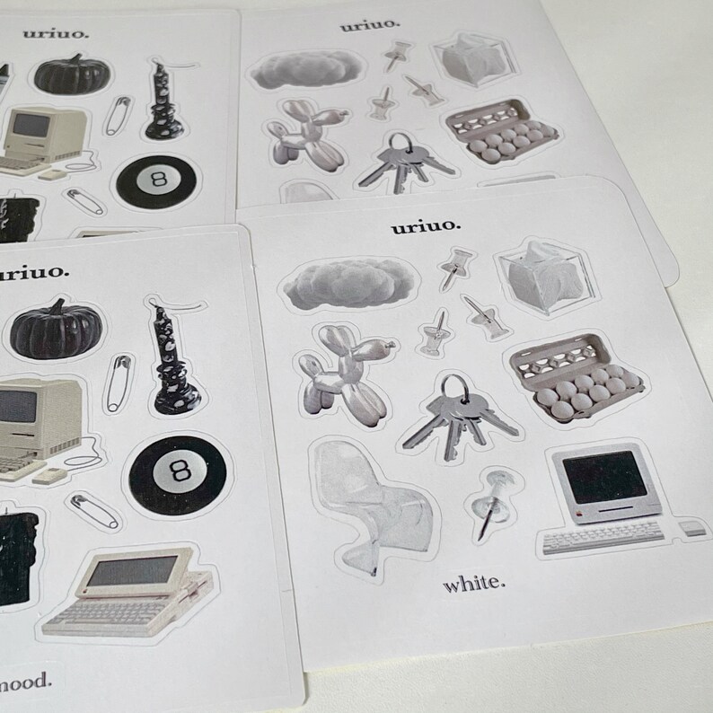 Puede incluir: Un conjunto de pegatinas con varias ilustraciones en blanco y negro, que incluyen una computadora, una nube, un animal de globo, una silla, una vela, una llave, una caja de huevos y una bola negra de 8. Las pegatinas est&aacute;n en hojas de papel blancas con el texto "uriuo." y "white." impreso en ellas.