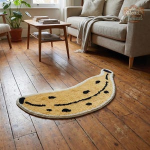 May include: A yellow banana-shaped rug with black spots and a smiling face design. The rug is placed on a wooden floor in a living room setting. The rug adds a playful touch to the room's decor.