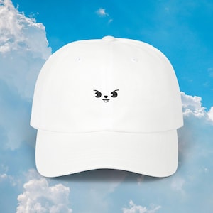 May include: White baseball cap with a curved brim and an embroidered cartoon face. The cap features a six-panel design with a button on top. The cartoon face has black eyes and a mouth, giving it a playful look.