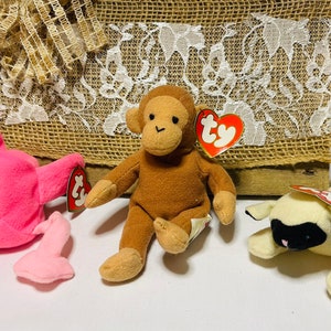 May include: Three plush toys: a pink flamingo, a brown monkey, and a white lamb. Each toy has a red Ty tag attached.