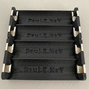 Può includere: Organizzatore di chiavi in ​​plastica nera con quattro slot. Ogni slot ha le parole "Paul E. Key" in rilievo sul davanti.