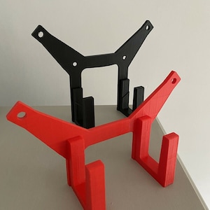 May include: Two 3D printed wall mounts, one red and one black, with a hook design. The mounts are stacked on top of each other.