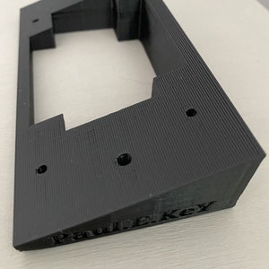 Könnte beinhalten: Eine schwarze Wandhalterung aus Kunststoff mit fünf Löchern und dem Text "Pawlkey" auf der Unterseite.