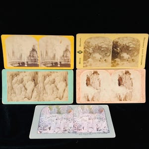 Op de afbeelding: Een verzameling vintage stereoscopische kaarten met winterlandschappen. De kaarten tonen ijzige watervallen en besneeuwde scènes, met verschillende gekleurde randen. De kaarten zijn gerangschikt op een zwart oppervlak.
