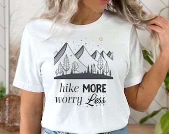May include: White t-shirt with a black and white graphic of mountains, trees, and a sun. The text "hike more worry less" is printed below the graphic.
