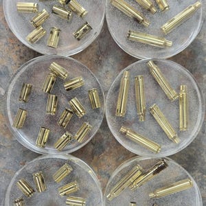May include: Six clear round coasters with gold bullet casings embedded in the resin. The coasters are arranged in two rows of three.