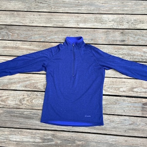 May include: A long-sleeved, blue, quarter-zip pullover shirt with a blue fleece lining. The shirt has a small "Patagonia" logo on the bottom right.