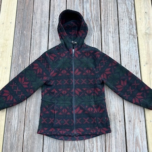 Puede incluir: Una chaqueta de forro polar negra con un patrón geométrico rojo y verde. La chaqueta tiene capucha y cierre de cremallera.