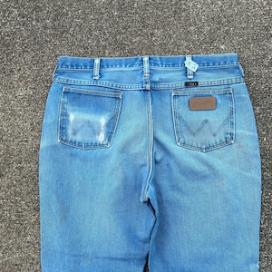 May include: A pair of blue denim jeans with a brown leather patch on the back pocket. The jeans have a faded look and are made of a soft, comfortable material.