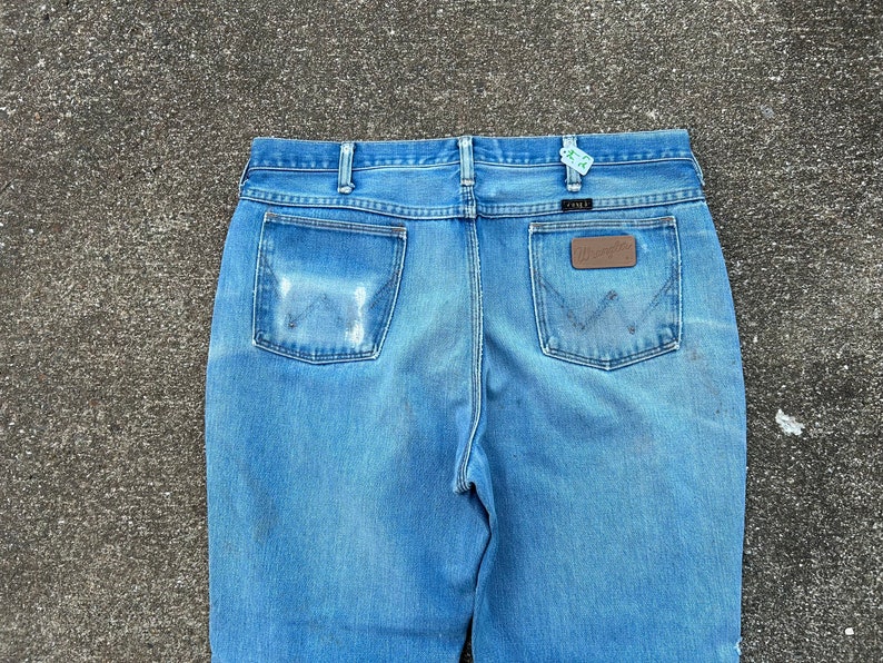 May include: A pair of blue denim jeans with a brown leather patch on the back pocket. The jeans have a faded look and are made of a soft, comfortable material.