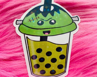 Op de afbeelding: Een holografische sticker van een bubble tea beker in de vorm van een groen monster. De beker heeft een groen deksel met een litteken, een rietje en donkere boba-parels aan de binnenkant. Het ontwerp bevat een lachend gezicht met kleine ogen.