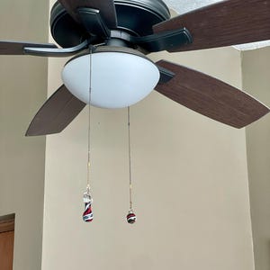 May include: A ceiling fan with dark brown blades and a white globe light. Decorative pull chains with red, black, and white accents hang from the light fixture, adding a touch of style to the room.