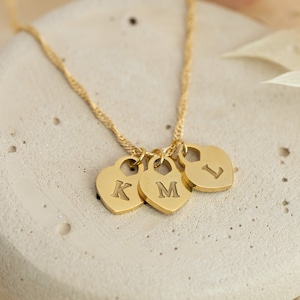 May include: Gold necklace with three heart-shaped charms, each with a letter engraved on it: K, M, and L.