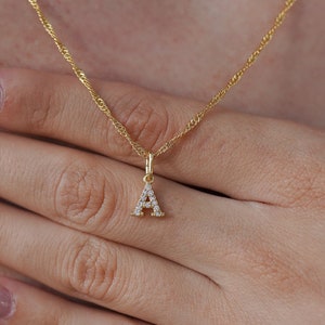 May include: A gold chain necklace with a small pendant in the shape of the letter A. The pendant is encrusted with small, clear stones.