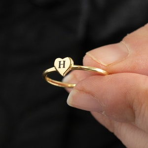 May include: A gold heart-shaped ring with the letter "H" engraved on the front.