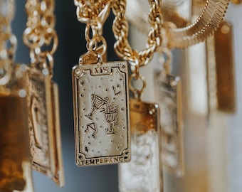 May include: Gold chain necklace with multiple charms featuring tarot card designs. The charms are rectangular and feature etched images of tarot cards. One charm reads "XIV TEMPERANCE".