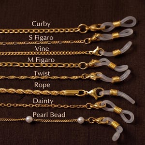 May include: Gold-toned eyeglass chains in various styles, including Curby, S Figaro, Vine, M Figaro, Twist, Rope, Dainty, and Pearl Bead. Each chain features a loop to attach to glasses and is displayed against a dark brown background.