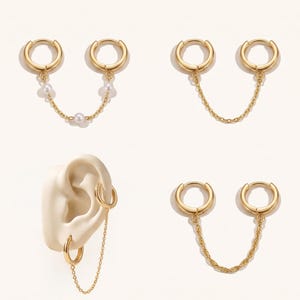 May include: A collection of gold-toned hoop earrings connected by delicate chains. One set features small white pearls along the chain, while others display plain or twisted link chains. One earring set is shown attached to a model ear form.