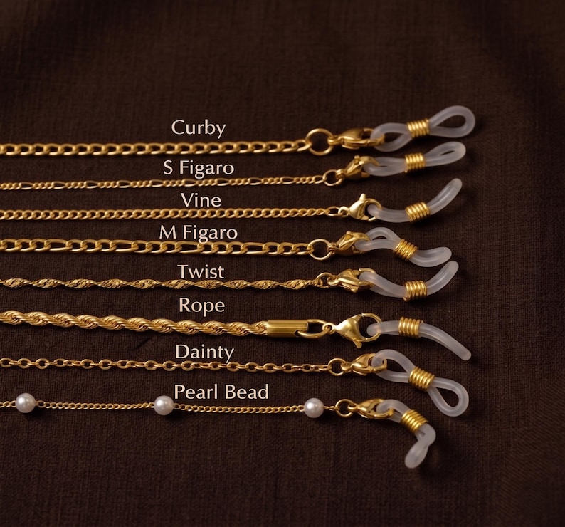 May include: Gold-toned eyeglass chains in various styles, including Curby, S Figaro, Vine, M Figaro, Twist, Rope, Dainty, and Pearl Bead. Each chain features a loop to attach to glasses and is displayed against a dark brown background.