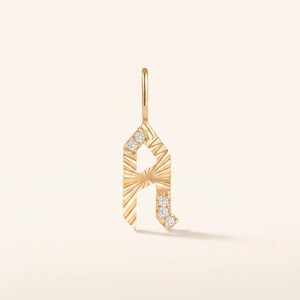 May include: A gold pendant shaped like the letter A, featuring a sunburst engraved texture across its surface. The pendant is accented with five small, clear round-cut stones embedded along the left and right vertical bars.