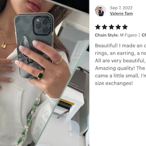 May include: A close-up of a person's hands wearing gold rings and a necklace with a small padlock charm. The person is holding a white iPhone with a marble-patterned case. The image includes a review with the text "Chain Style: M Figaro | Chain Length: 17 inches Beautiful! I made an order of 5 different rings, an earring, a necklace and an anklet. All are very beautiful, very yellow gold! Amazing quality! The only issue is the anklet came a little small, I'm hoping they accept size exchanges!"