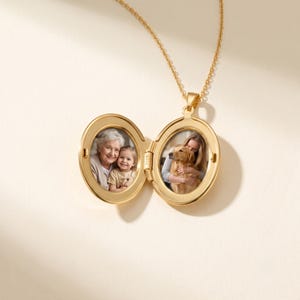 May include: A gold-toned oval locket pendant suspended from a matching delicate chain. The locket is open, revealing two interior compartments. The left side displays a photograph of an older adult and a child, while the right side shows a photograph of a person embracing a golden dog.