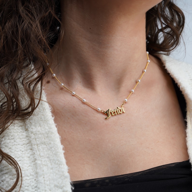 K&ouml;nnte beinhalten: Eine goldene Halskette mit einer Perlenkette und einem Namensschild-Anh&auml;nger mit der Aufschrift "Jendi".